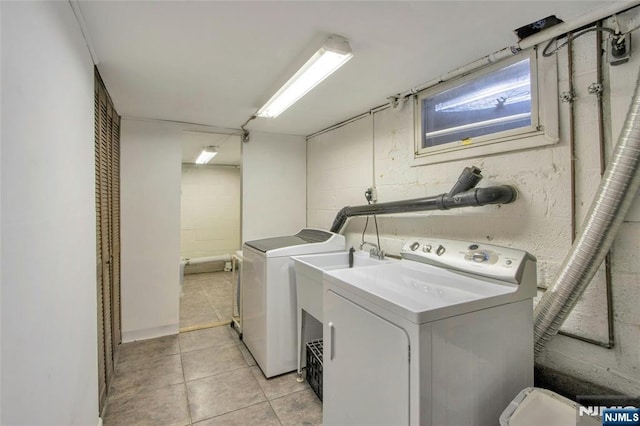 washroom featuring concrete block wall, laundry area, washing machine and dryer, and light tile patterned floors