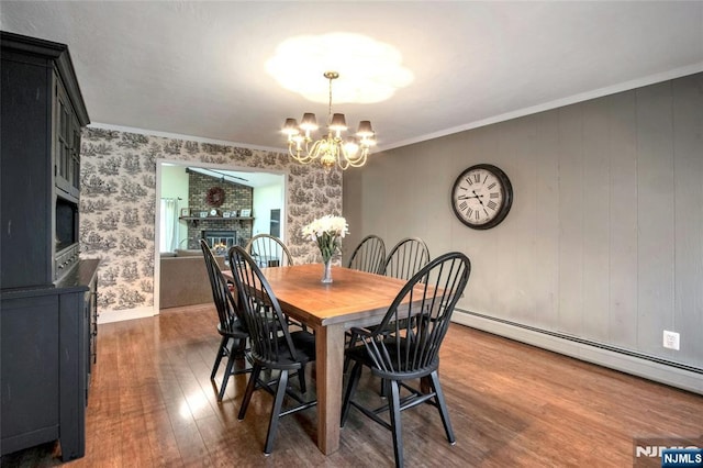 dining area featuring a chandelier, a baseboard heating unit, wood finished floors, ornamental molding, and a glass covered fireplace