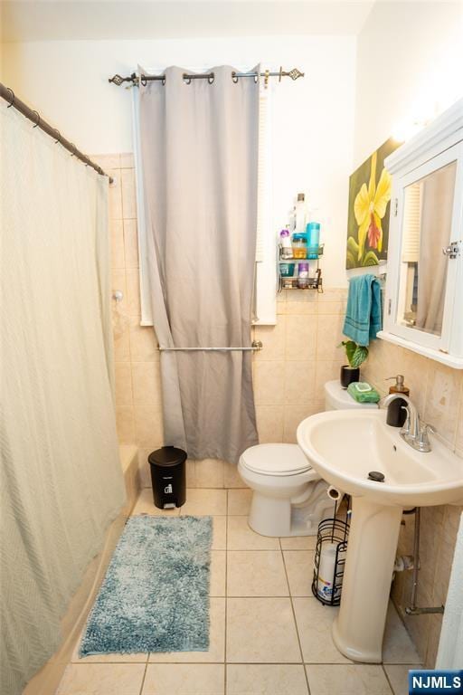 bathroom featuring wainscoting, toilet, a shower with curtain, tile patterned floors, and tile walls