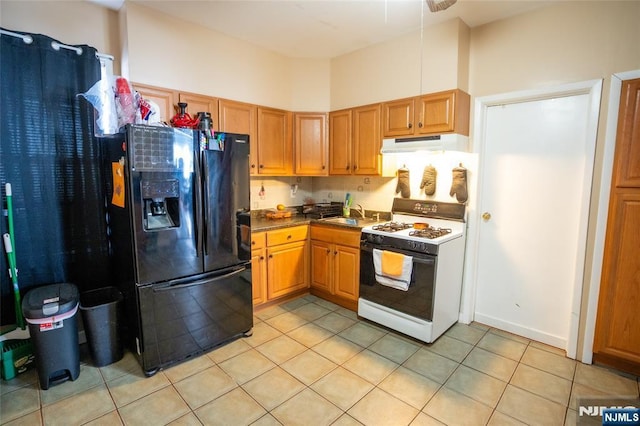 kitchen featuring light tile patterned floors, black fridge with ice dispenser, a sink, white range with gas stovetop, and under cabinet range hood