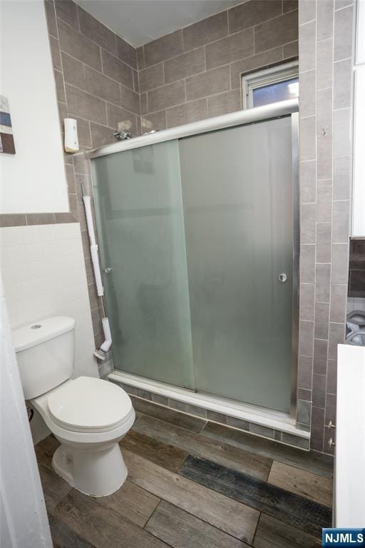 full bath with toilet, tile walls, a shower stall, and wood finished floors