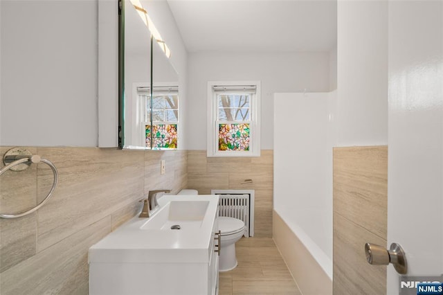 bathroom featuring toilet, vanity, tile walls, wainscoting, and radiator