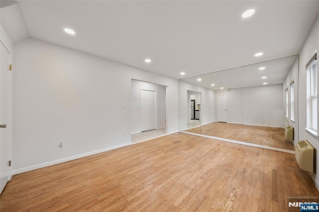 empty room featuring light wood-style flooring, a wall mounted air conditioner, baseboards, and recessed lighting