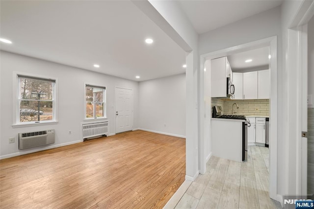 unfurnished living room with light wood finished floors, recessed lighting, radiator heating unit, a wall mounted AC, and baseboards