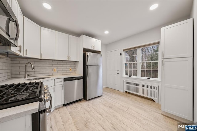 kitchen with decorative backsplash, radiator, stainless steel appliances, white cabinetry, and a sink