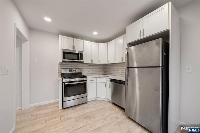 kitchen featuring stainless steel appliances, tasteful backsplash, light wood-style flooring, white cabinets, and a sink