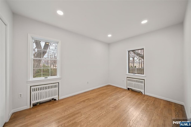 unfurnished room with light wood-type flooring, radiator heating unit, and a wealth of natural light