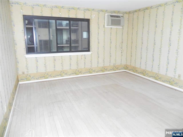 unfurnished room featuring wallpapered walls, baseboards, wood finished floors, and a wall mounted air conditioner