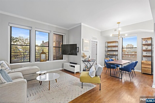 living area with a healthy amount of sunlight, an inviting chandelier, crown molding, and wood finished floors