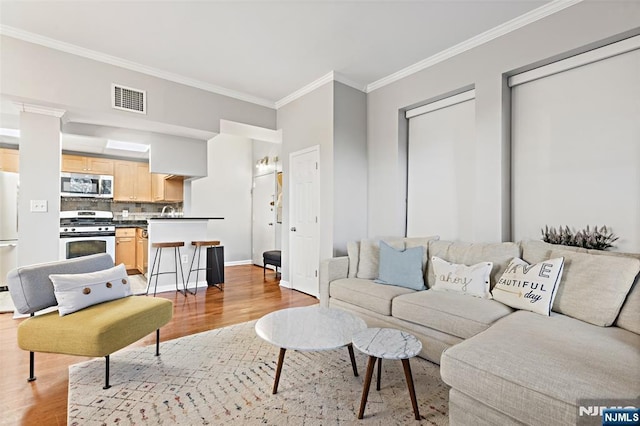 living room with ornamental molding, light wood-style flooring, visible vents, and baseboards
