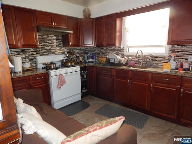 kitchen with a sink, under cabinet range hood, white gas range, decorative backsplash, and reddish brown cabinets