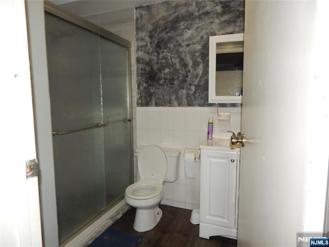 bathroom with wallpapered walls, a wainscoted wall, toilet, a stall shower, and tile walls