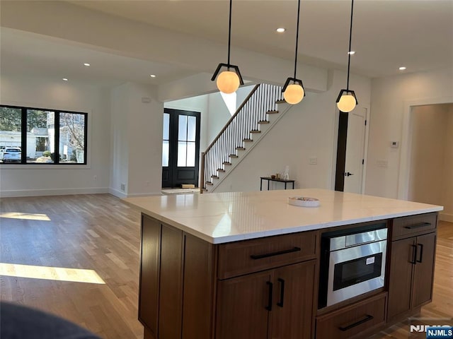 kitchen with stainless steel microwave, baseboards, open floor plan, recessed lighting, and light wood-style flooring