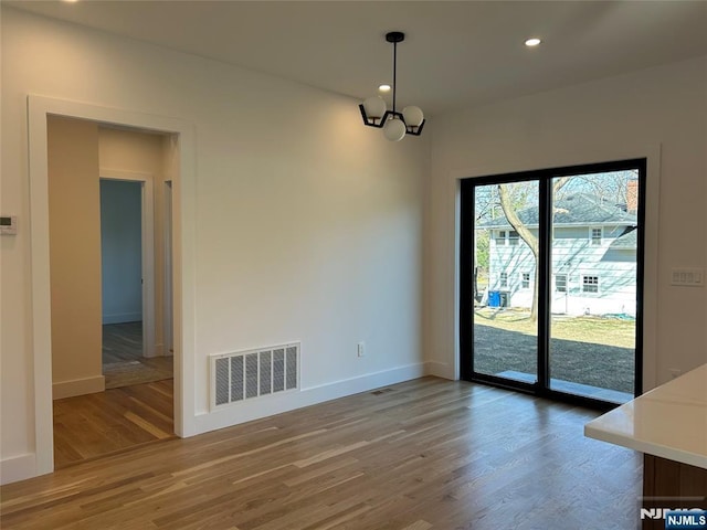 unfurnished dining area with a notable chandelier, wood finished floors, visible vents, and baseboards