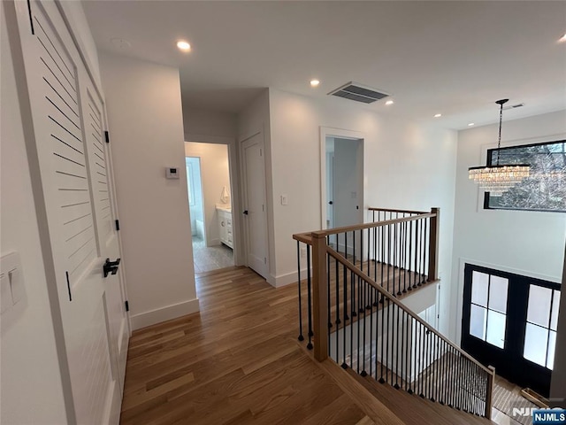 hallway with visible vents, an upstairs landing, a notable chandelier, wood finished floors, and recessed lighting