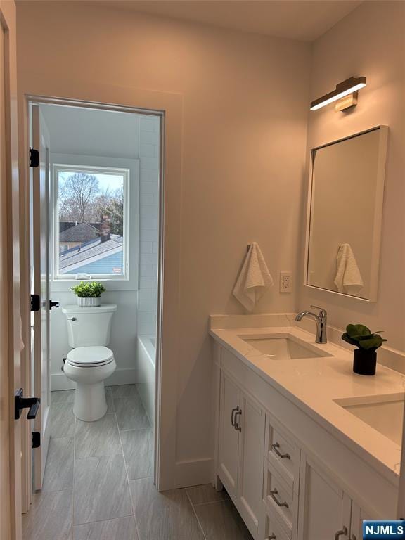 bathroom with double vanity, toilet, a tub to relax in, and a sink