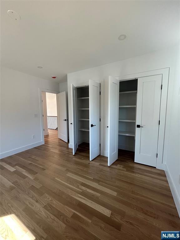 unfurnished bedroom featuring wood finished floors, baseboards, and two closets