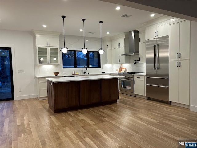 kitchen with high end appliances, light countertops, white cabinets, light wood-style floors, and wall chimney exhaust hood