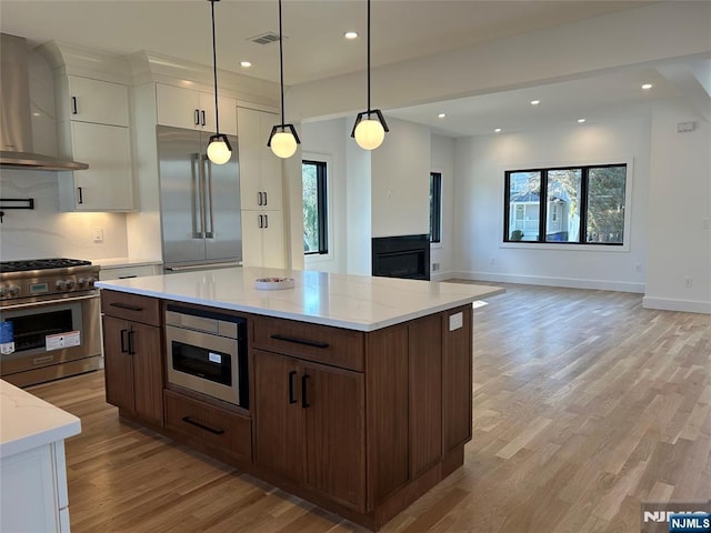 kitchen with visible vents, white cabinets, light wood-style floors, built in appliances, and wall chimney exhaust hood