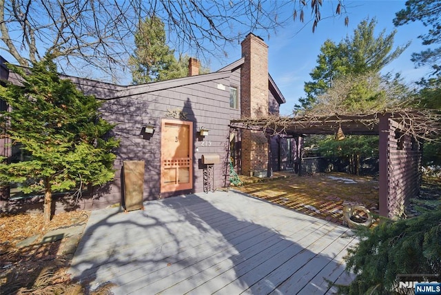 back of house with a chimney, a wooden deck, and a pergola