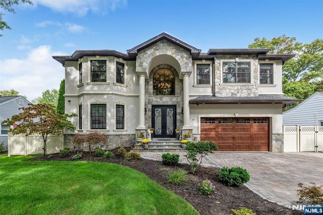 view of front of house featuring stone siding, french doors, decorative driveway, and fence