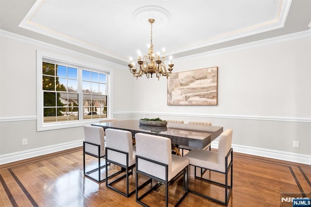 dining area featuring a notable chandelier, crown molding, a raised ceiling, wood finished floors, and baseboards