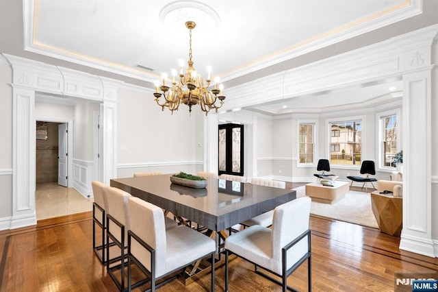 dining space with ornate columns, wood-type flooring, a raised ceiling, and a decorative wall