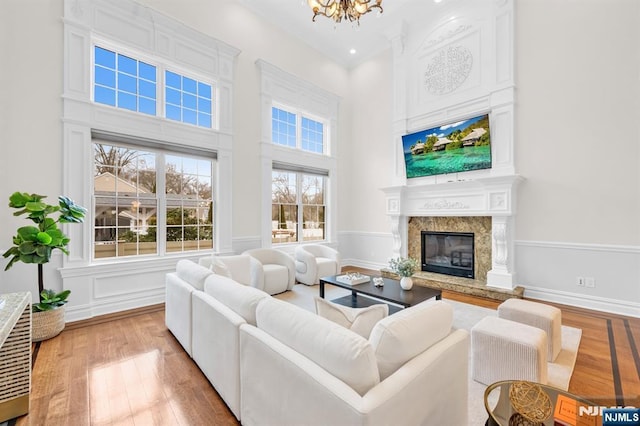 living room with a towering ceiling, light wood-style floors, a fireplace, and a notable chandelier