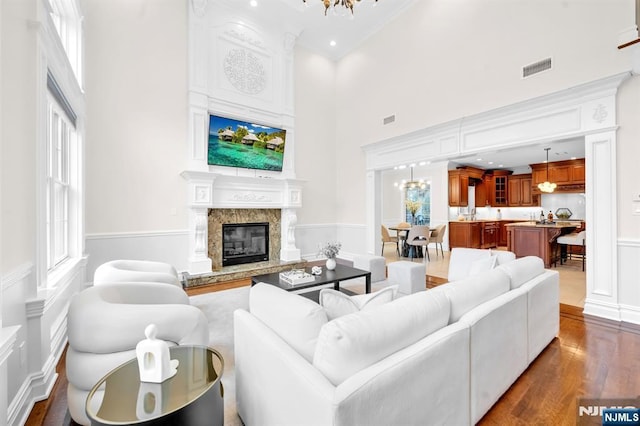 living area featuring visible vents, a decorative wall, a premium fireplace, dark wood-type flooring, and a chandelier