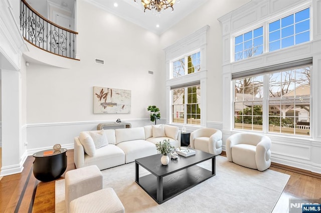 living area featuring visible vents, a towering ceiling, ornamental molding, wood finished floors, and a chandelier