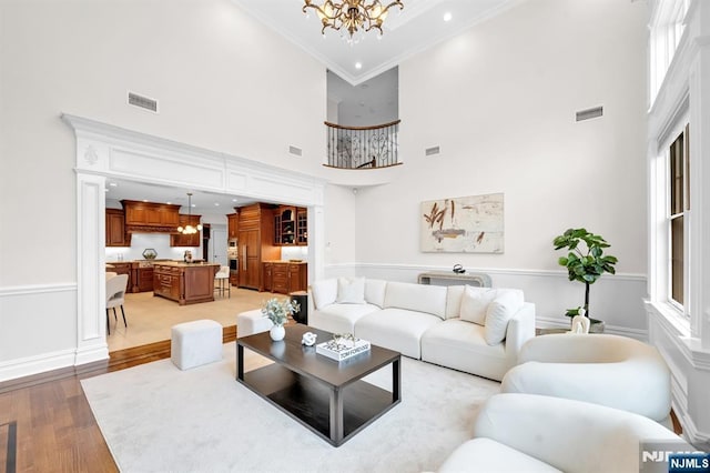 living room featuring ornamental molding, visible vents, a notable chandelier, and light wood finished floors