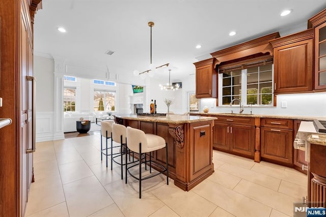 kitchen with a kitchen island, a sink, open floor plan, light stone countertops, and a kitchen bar