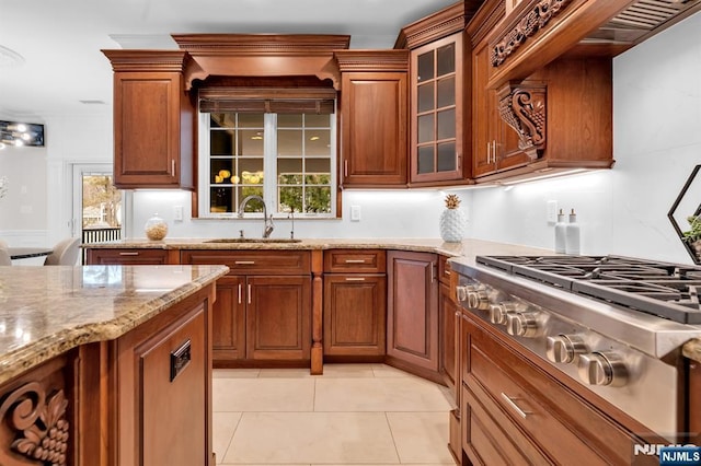 kitchen with light stone countertops, stainless steel gas stovetop, brown cabinets, and a sink