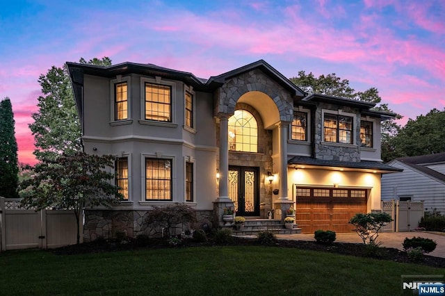 view of front of house with stone siding, an attached garage, fence, and stucco siding