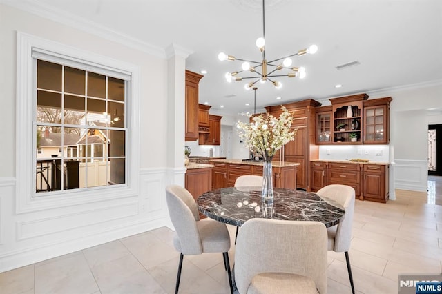 dining area featuring an inviting chandelier, visible vents, a decorative wall, and crown molding