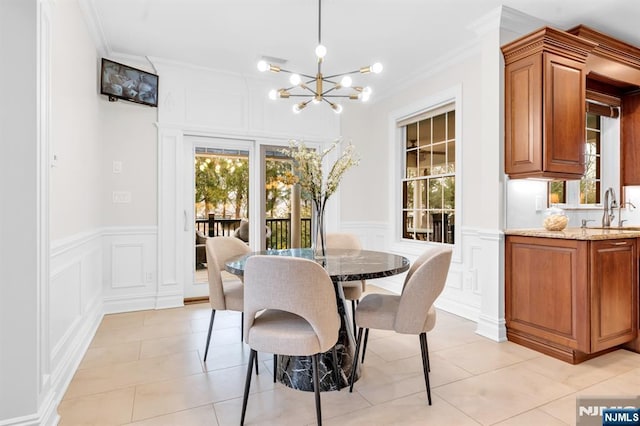 dining room with a wainscoted wall, ornamental molding, an inviting chandelier, a decorative wall, and light tile patterned flooring