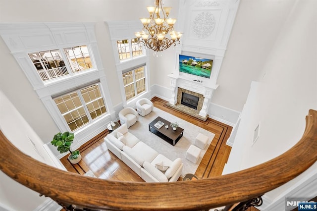 living area featuring a notable chandelier, wood finished floors, a towering ceiling, baseboards, and a high end fireplace