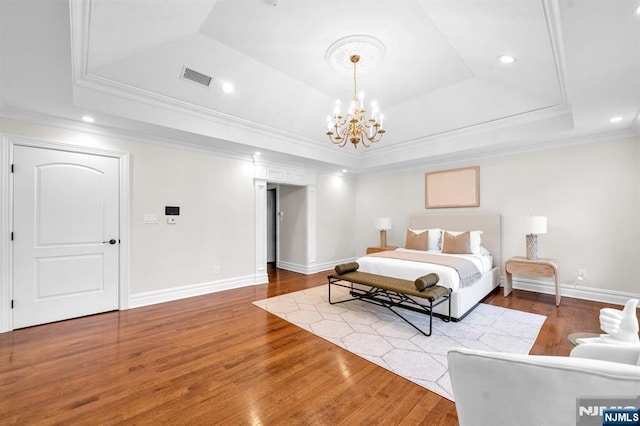 bedroom featuring visible vents, wood finished floors, a tray ceiling, crown molding, and a notable chandelier