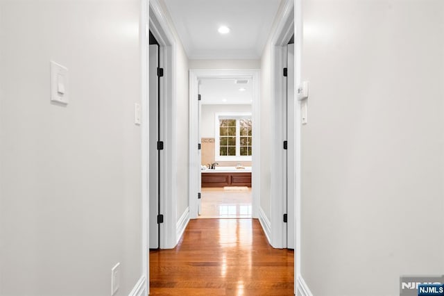 hallway with baseboards, ornamental molding, and wood finished floors