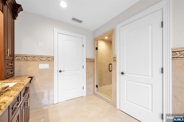 full bathroom featuring visible vents, a wainscoted wall, vanity, a shower stall, and tile walls