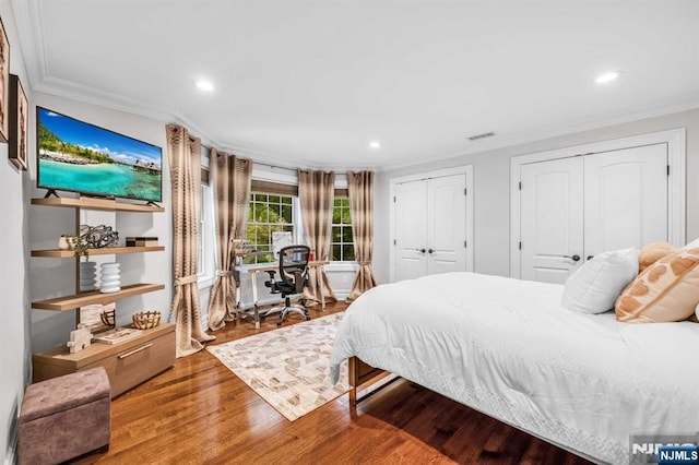 bedroom featuring wood finished floors, visible vents, crown molding, and two closets