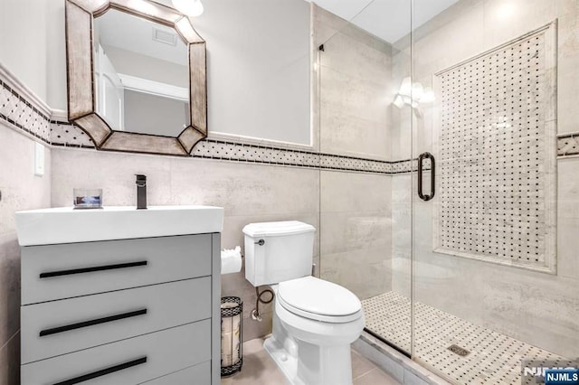 bathroom featuring toilet, a stall shower, vanity, and tile walls