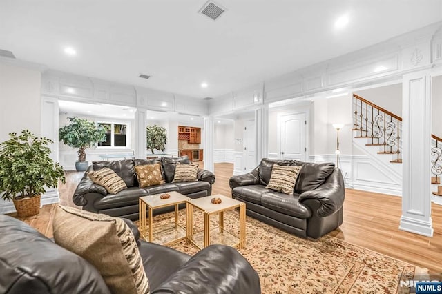 living area featuring light wood-type flooring, stairs, visible vents, and a decorative wall