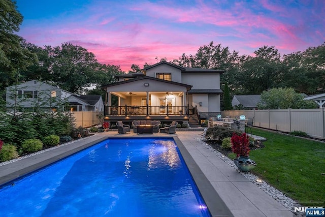 back of house at dusk with a fenced in pool, a fenced backyard, ceiling fan, a yard, and stucco siding