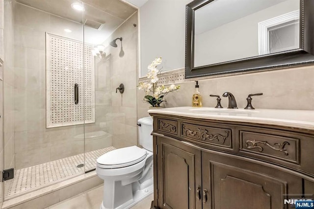 full bath with tile walls, toilet, wainscoting, a shower stall, and vanity