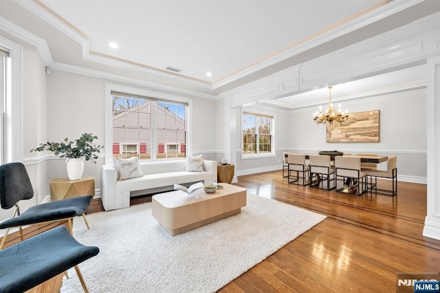 living room featuring wood-type flooring, ornamental molding, a tray ceiling, a notable chandelier, and recessed lighting