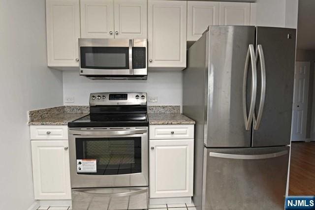 kitchen featuring stainless steel appliances, light stone countertops, white cabinets, and light wood finished floors