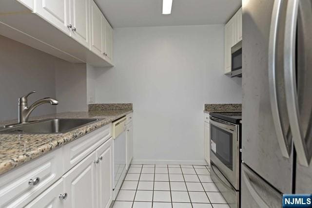 kitchen featuring a sink, white cabinetry, stainless steel appliances, light tile patterned flooring, and baseboards