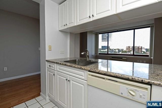 kitchen with a sink, light stone countertops, white cabinets, and white dishwasher