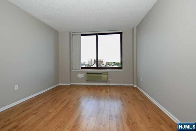 spare room featuring baseboards, a textured ceiling, light wood-style flooring, and a wall unit AC